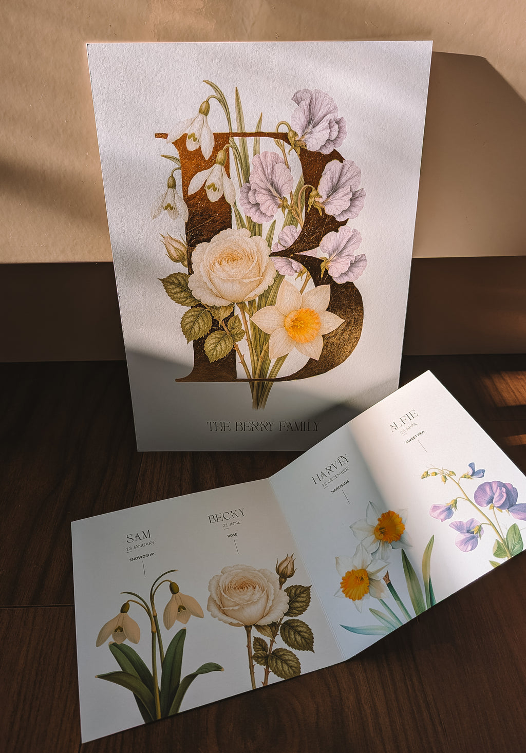 A set of personalised botanical art featuring vintage-style illustrations of flowers and leaves, arranged on a dark wooden surface with a beige wall in the background.
