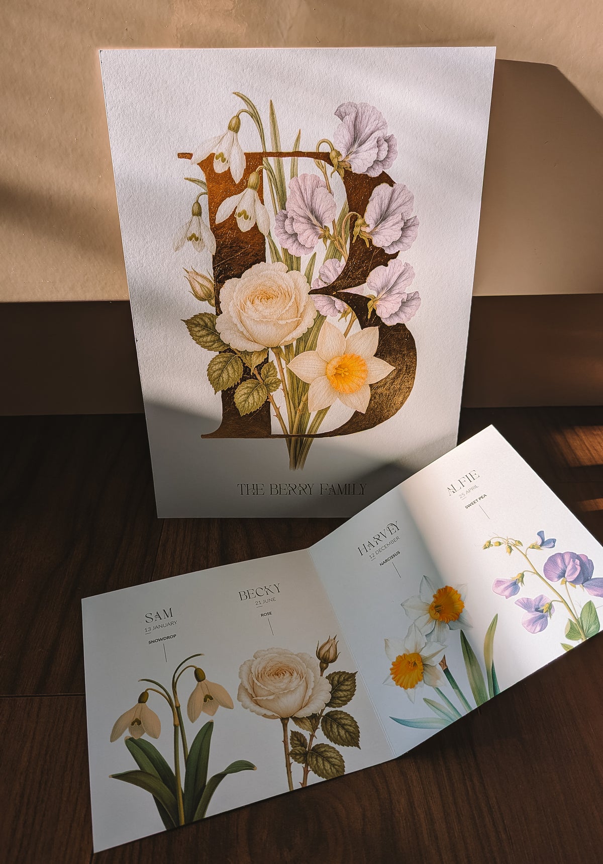 A set of personalised botanical art featuring vintage-style illustrations of flowers and leaves, arranged on a dark wooden surface with a beige wall in the background.