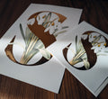 Print & card featuring a large decorative letter 'S' filled with white snowdrop flowers and green leaves, arranged on a dark wooden surface.